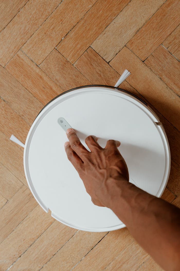 Close-up of a hand interacting with a robot vacuum cleaner on a parquet floor, showcasing modern cleaning technology.